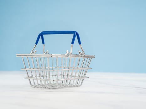 An empty mini shopping cart over a marble floor with a light blue background photo