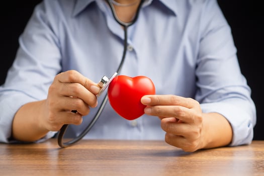 A doctor hand holding a stethoscope checking a red heart shape while sitting in the hospital or clinic photo