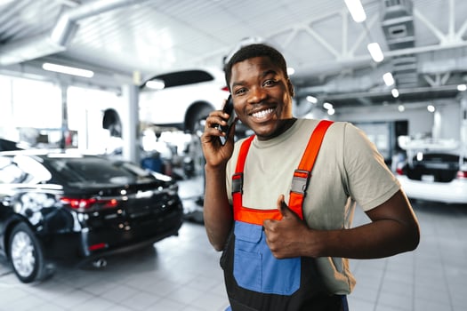 Young African mechanic man wearing uniform using mobile phone in a car service photo