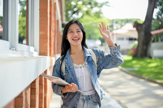 A cheerful Asian female college student waves to her friends while walking on her way to class. photo