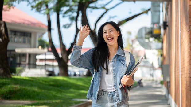 A cheerful Asian female college student waves to her friends while walking on her way to class. photo