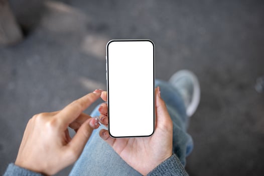 A top view of a woman sitting outdoors, holding a smartphone with a white screen mockup. photo