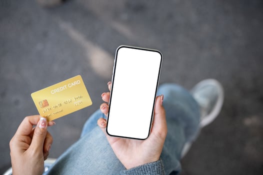 A top view of a woman sitting outdoors, holding a credit card and a smartphone with a screen mockup. photo