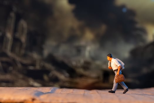 Miniature figures carrying luggage walk against a somber backdrop, symbolizing displacement and the human cost of war photo