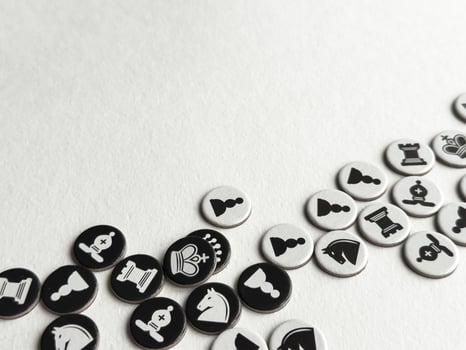 Chess themed tokens on white surface. Strategic game pieces in black and white photo