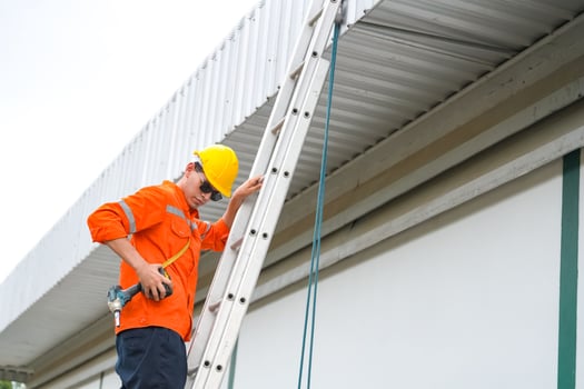 A man in an orange shirt and safety vest is climbing a ladder photo