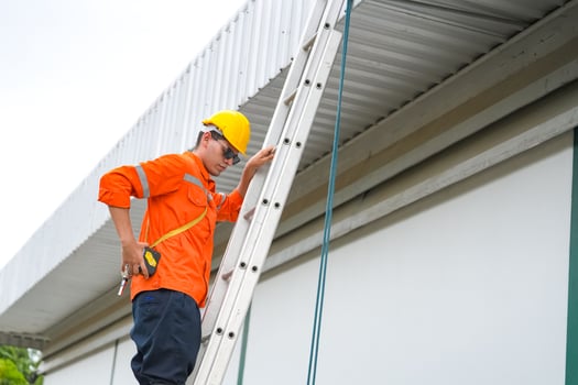 A man in an orange shirt and safety glasses on a ladder photo