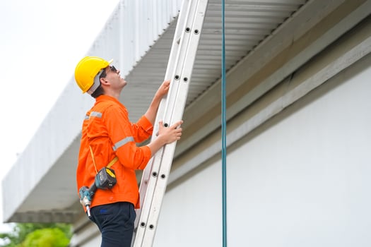 A man in an orange shirt and hard hat is climbing a ladder photo