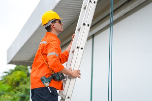 A man in an orange shirt and hard hat is standing on a ladder photo