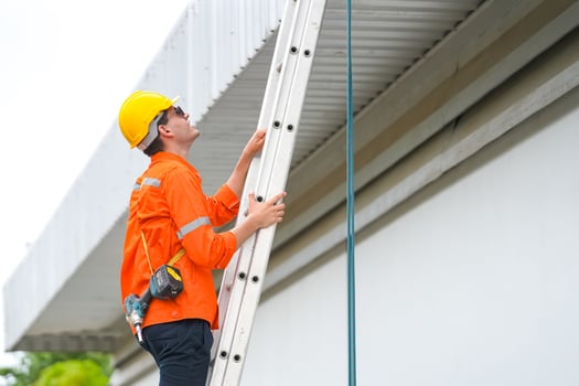 A man in an orange shirt and hard hat is climbing a ladder photo