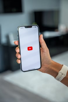 Prague, Czech republic - May 2, 2024. Woman holding iPhone with logo of application YouTube on the screen, using mobile application for business home. High quality photo