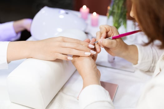 Ladies indulge in a relaxing manicure at a salon, with one woman receiving nail art while candles create a calming atmosphere. The focus is on vibrant nails and attentive service. photo