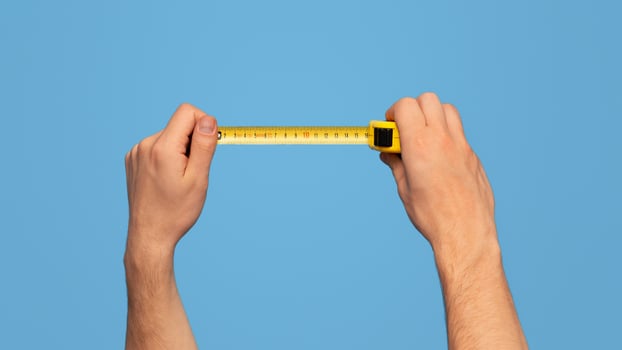 Handyman holding tape measure on blue background, closeup view. Panorama photo