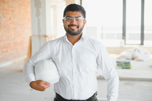 Indian construction site manager standing wearing helmet, thinking at construction site. Portrait of mixed race manual worker or architect photo