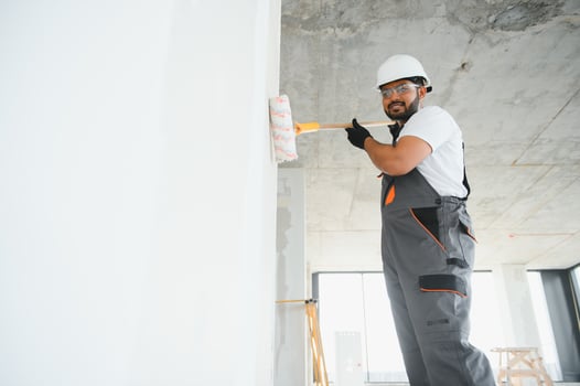 An Indian apartment repair worker paints a white wall with a roller photo