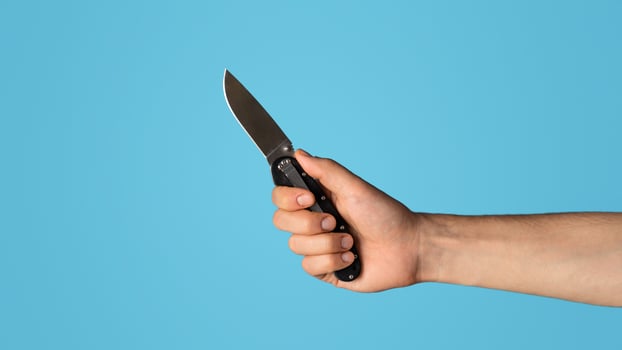 Close up of young guy holding pocket knife on blue background, blank space. Panorama photo
