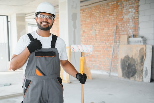 An Indian apartment repair worker paints a white wall with a roller photo
