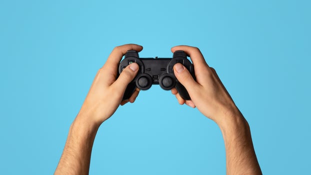 Stay home activities. Young guy holding joystick, playing games on blue background, closeup. Panorama photo