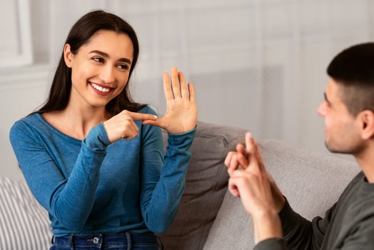 Smiling deaf and mute couple communicating at home using sign language, sitting on couch in living room photo