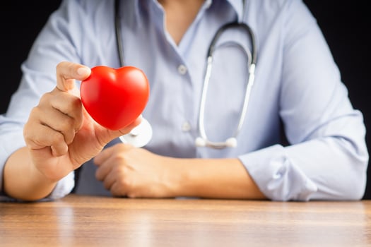 Cardiology concept. Close-up of hand doctor holding a red heart shape while sitting in the hospital photo