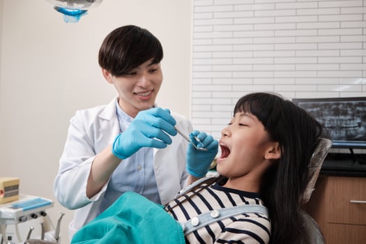 A young Asian male pediatric dentist checks and examines a little Thai girl's teeth in dental clinic, well-being mouth oral hygiene, and professional orthodontic healthcare work in a kid hospital. photo