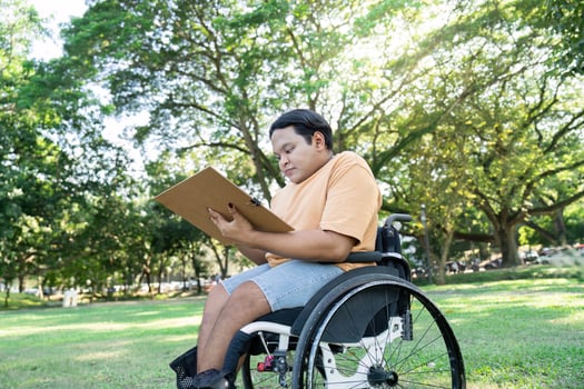 Young Artist in Wheelchair Drawing Outdoors in Sunny Park Surrounded by Lush Greenery and Trees photo