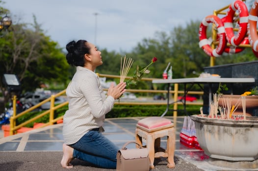 Woman Asia kneels in prayer, holding incense sticks and rose, expressing her devotion at spiritual altar, surrounded by elements of nature and tranquility photo