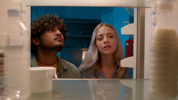 Point of view POV inside refrigerator Caucasian girl woman girlfriend wife and Arabian man Indian guy boyfriend husband multiracial couple at night evening open empty fridge at kitchen unhappy sad photo