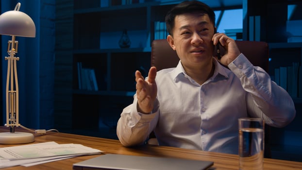 Happy Asian man worker manager executive boss entrepreneur at night office talking mobile phone at desk. Korean businessman Chinese company CEO Japanese investor talk smartphone call at late evening photo
