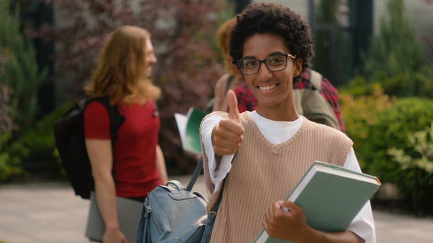 Students talking near university campus outdoors African American happy satisfied student girl woman showing thumb up like recommend gesture after class education with book good high school knowledge photo