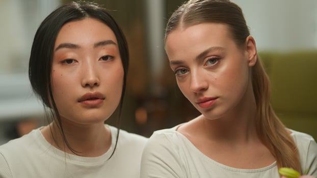 Two beautiful healthy multiracial girls floral bloom organic cosmetic aroma perfume cosmetology make-up multiethnic females women Asian woman girl Caucasian holding flowers near faces skin care beauty photo