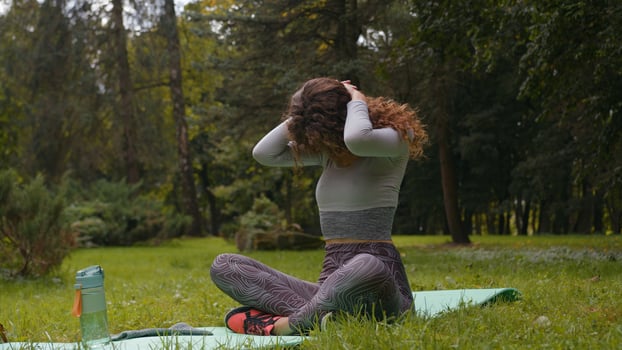 Sportive slim woman outdoors in park stretch neck muscles lower head down stretching back warm up before fitness exercise workout training yoga practice girl at nature sporty female sport sit at mat photo