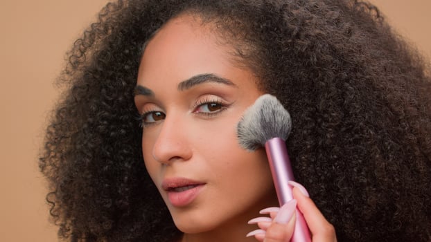 Close up portrait at beige studio background beautiful African American woman attractive ethnic girl looking at camera apply powder for face make-up preparing cosmetics beauty blush bronzer contouring photo
