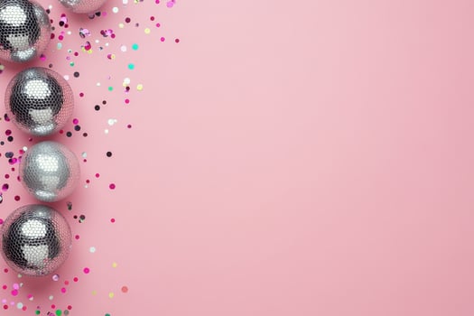 Shimmering disco balls glisten on a pink surface with confetti scattered around photo