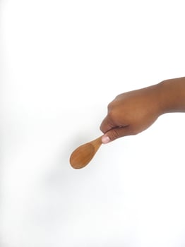 The image shows a hand holding a round wooden spoon with a smooth surface. The plain white background emphasizes the natural texture and grain patterns of the wood, making the bowl the central focus. photo