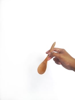 The image shows a hand holding a round wooden spoon with a smooth surface. The plain white background emphasizes the natural texture and grain patterns of the wood, making the bowl the central focus. photo