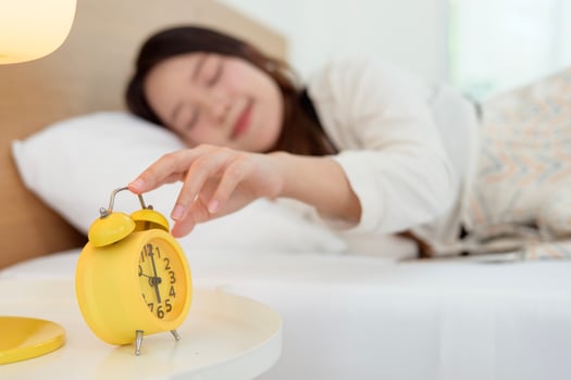Sleeping asian woman turning off alarm on clock while being Waken up in the morning photo