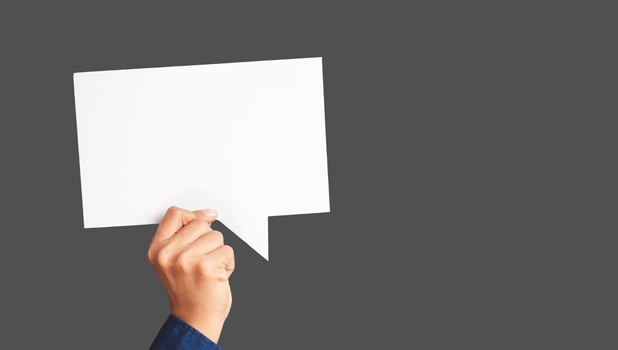 Close-up of hand holding a white speech bubble against a gray background photo