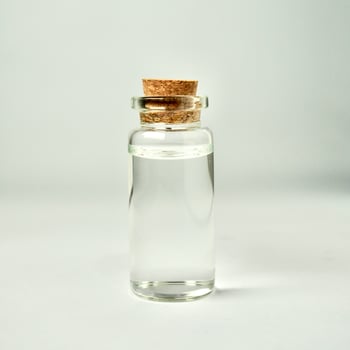 One transparent glass vial bottle container with brown cork stopper lid isolated on square white background. photo