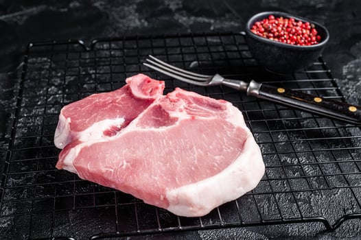 Uncooked Raw pork T bone chop meat steak on grill. Black background. Top view photo