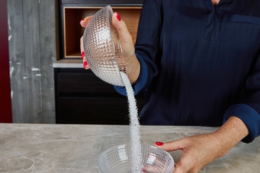 Hands pouring sushi vinegar mixture over cooked rice in a bamboo bowl, highlighting a key step in making sushi. photo