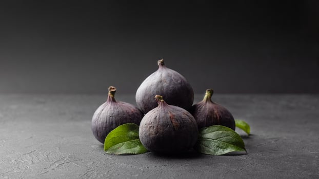 Fresh figs and green leaves on a black texture background, health and diet food. selective focus photo