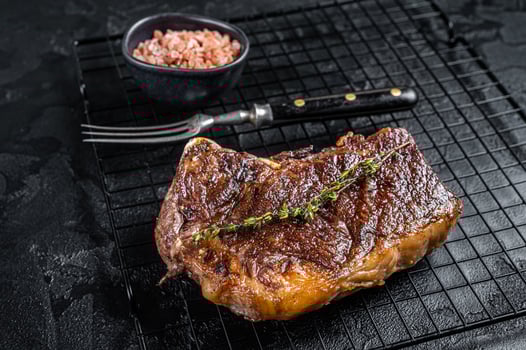 Grilled Striploin beef meat steak or new york steak on a grill rack. Black background. Top view photo
