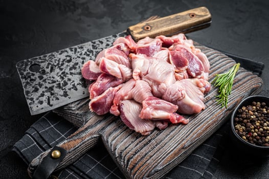 Raw chicken stomachs, giblets gizzards on a butcher board with meat cleaver. Black background. Top view photo