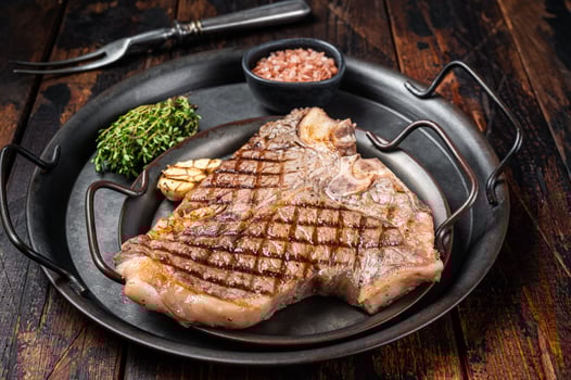 BBQ Grilled T-bone or Porterhouse beef meat Steak on a steel tray with herbs. Wooden background. Top view photo