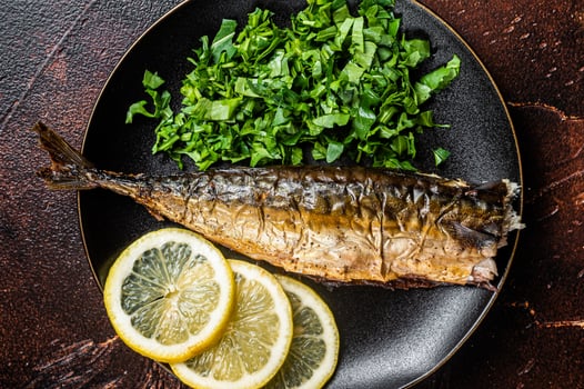 Grilled Mackerel Scomber fish on a plate with greens and lemon. Dark background. Top view photo