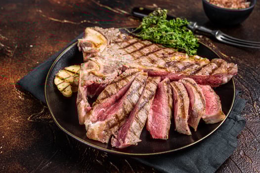 Grilled Medium rare Porterhouse, T-Bone Steak sliced in a plate. Dark background. Top view photo
