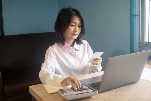 Asian female using laptop paying bill online for calculating managing personal banking finance at home photo