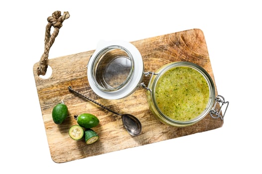 Green feijoa jam on a wooden chopping Board in a glass jar. Isolated on white background. Top view. photo