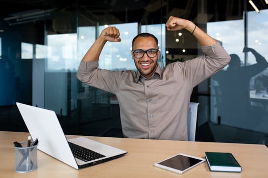 Happy man working in office showing muscles raising arms up, happy at workplace, smiling and looking at camera. photo
